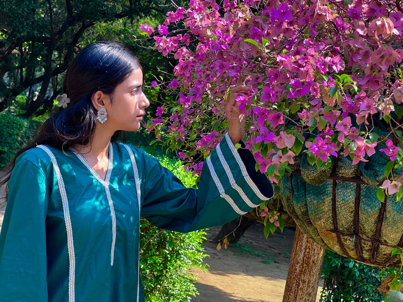Teal Green Kurta with Rainbow Silver Lace Detailing – Side Pose Woman wearing a teal green kurta with rainbow silver lace detailing and flared sleeves beside pink flowers in a garden