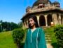 Close-up view of a woman wearing a teal green kurta with a V-neckline and rainbow silver lace trim in a garden
